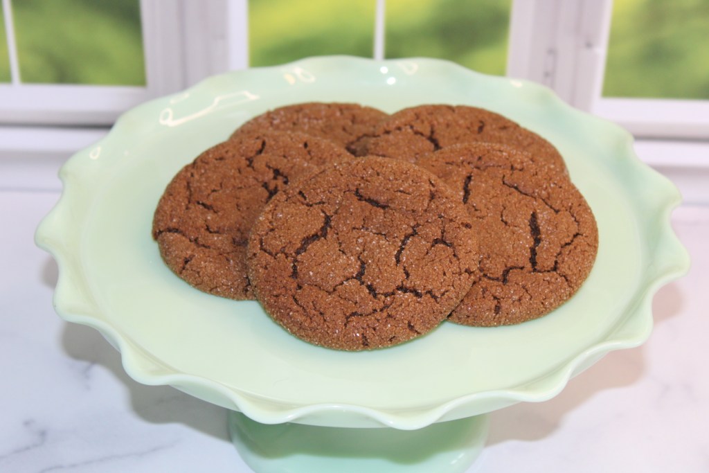 A plate of freshly baked ginger cookies displayed on a green cake stand with a blurred window background.